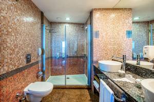 Ein Badezimmer mit einer Glasdusche, zwei Waschbecken, einem Spiegel und einem Toilettensitz im Asteria Family Resort Belek.