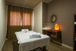Spa-Behandlungsraum im VOI Praia De Chaves Resort mit einer Massageliege, einem Waschbecken, einem Spiegel und einer Lampe.