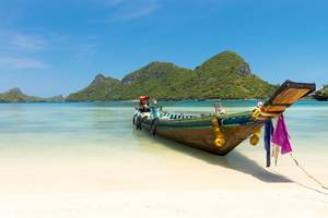 Ein Boot liegt am Strand von Koh Phangan mit Bergen im Hintergrund.