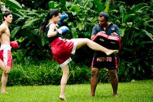 Drei Personen machen Muay Thai Training im Freien, einer kickt während zwei andere zuschauen.