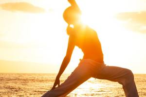 Person praktiziert Yoga am Strand bei Sonnenaufgang mit Blick auf das Meer