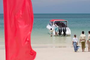 Familie am Strand von Anantara Rasananda Koh Phangan Villas mit einem Boot im Hintergrund