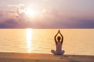 Frau praktiziert Yoga auf dem Strand bei Sonnenuntergang