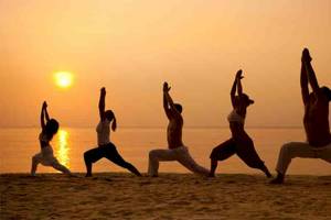 Mehrere Personen praktizieren Yoga auf dem Strand bei Sonnenuntergang.