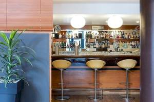 Die Bar im NH Hamburg Altona Hotel mit runden Barhockern und einer grünen Pflanze.