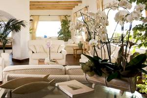 Wohnbereich im Colonna Grand Hotel Capo Testa mit weißen Möbeln, Pflanzen und einem Glastisch.