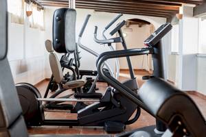 Fitnessbereich im Colonna Grand Hotel Capo Testa mit mehreren Geräten wie Laufbändern und Rudergeräten.