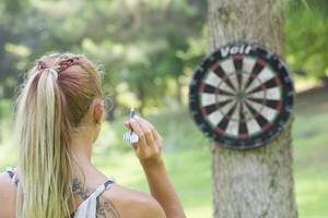 Frau wirft Dart auf eine Scheibe, die an einem Baum befestigt ist.