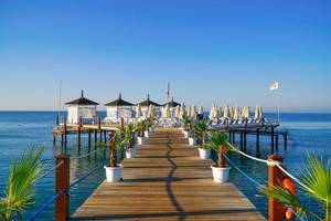 Anlegepier des Baia Lara Hotels mit Strandschirmen und Palmen an einem sonnigen Tag