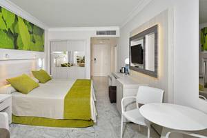 Innenansicht eines Hotelzimmers im Sol Palmeras Hotel mit grünem Bett und weißen Möbeln.