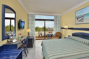 Innenansicht eines Hotelzimmers im Sol Palmeras Hotel mit Balkon, Fernseher, Schreibtisch und Gemälde.