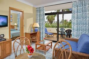 Innenansicht des Sol Palmeras Hotelzimmers mit Fernseher, Schreibtisch, Loungebereich und Balkon.