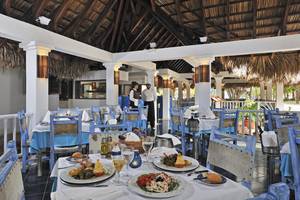 Restaurant im Sol Palmeras Hotel mit blauen Stühlen und Tischen, serviertem Essen und zwei Mitarbeitern im Hintergrund.