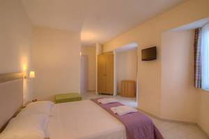 Ein geräumiges Hotelzimmer im Solimar Dias Hotel mit einem Bett, Kissen, Decken, einem Fernseher und einem Kleiderschrank.