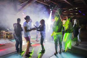 Mehrere Leute tanzen in einer Disco mit Lichteffekten und Rauch.
