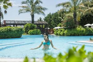 Frau in einem blauen Bikini schwimmt im Pool im Freien des Liberty Hotels Lara