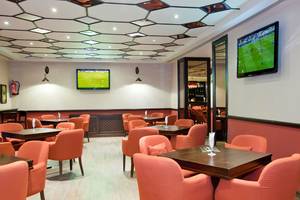 Innenansicht des Restaurants im Grand Waterworld Makadi Hotel mit orangefarbenen Stühlen und Tischen, Fernsehern an der Wand und einer gemusterten Decke.