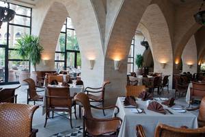 Restaurant im Grand Waterworld Makadi Hotel mit braunen Stühlen und Tischen, gerahmt von hohen Bögen.