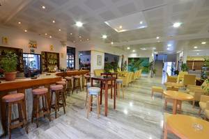 Die Lobby-Bar des Tropical Sol Hotels mit Barhockern, Tischen und gelb gepolsterten Stühlen.