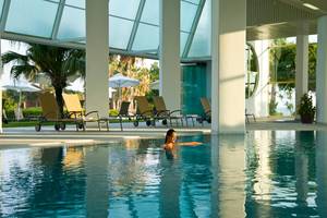 Frau schwimmt im Pool im Louis Imperial Beach Hotel mit Lounge-Sesseln und Palmen im Hintergrund.