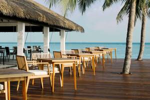 Außenterrasse des Noku Maldives Hotels mit Holztischen und Stühlen, Blick aufs Meer.