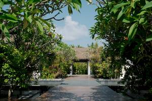 Eingang des Noku Maldives Hotels umgeben von tropischen Pflanzen und Bäumen.