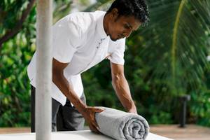 Mitarbeiter des Noku Maldives rollt ein Handtuch auf einer weißen Tischplatte.