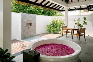 Außenbereich des Noku Maldives Hotels mit einer Badewanne voller Blumen und einem Tisch.