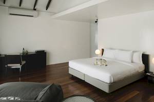 Innenansicht eines Schlafzimmers im Noku Maldives Hotel mit einem Bett, Nachttischen und Schreibtisch.