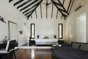 Innenansicht eines Schlafzimmers im Noku Maldives Hotel mit Bett, Sofa, Schreibtisch und Lampe.