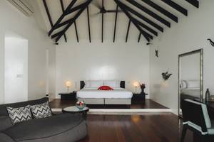Schlafzimmer im Noku Maldives Hotel mit hohem Dach, weißen Wänden und Holzboden.