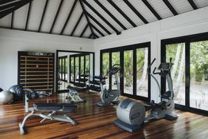 Innenansicht des Fitnesscenters im Noku Maldives Hotel mit Geräten und Fenstern.