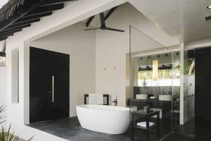 Badezimmer im Noku Maldives Hotel mit Badewanne, Glasdusche und schwarzen Türen.