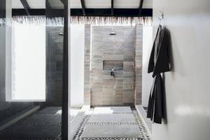 Dusche im Noku Maldives Hotel mit steinerner Wand und offenem Eingang.