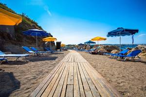 Strand des Kresten Palace Hotels mit Sonnenliegen und Sonnenschirmen an einem sonnigen Tag.