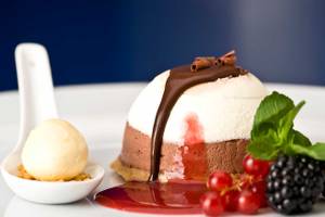 Ein Dessert mit Schokoladencreme, Beeren und Sahne auf einem weißen Teller.