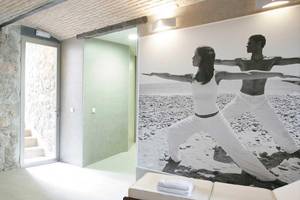 Innenansicht eines Yoga-Raums im Barcelo Illetas Albatros Hotel mit einer Steinwand und einem Foto von zwei Menschen in Yoga-Pose.