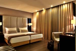 Doppelbettzimmer im Turim AV Liberdade Hotel mit goldenen Vorhängen und Schreibtisch.