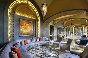 Lobby-Lounge-Bereich des Steigenberger Alcazar Hotels mit einer langen grauen Couch, mehreren Glastischen und einer großen Wandmalerei.