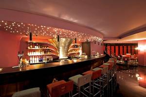 Innenansicht der Bar im Iberostar Grand Rose Hall Hotel mit voll ausgestatteter Theke und roten Barhockern.