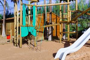 Kinderspielplatz im Freien mit Holzgerüsten, Rutschen und Schaukeln vor dem Servatur Waikiki Hotel.