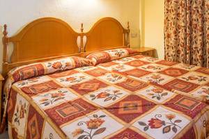 Doppelzimmer im Bluesea Callao Garden Hotel mit zwei Einzelbetten, Bettwäsche mit Blumenmuster, zwei Nachttischen und gelben Wänden.