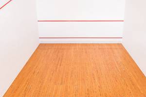Leere Squashhalle mit roten Linien auf weißen Wänden und einem hölzernen Boden.