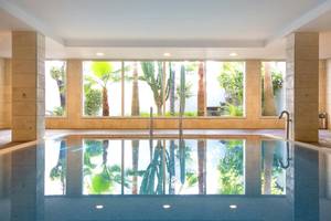Innenansicht des Swimmingpools im Hipotels Hipocampo Playa Hotel mit großen Fenstern und tropischen Pflanzen.