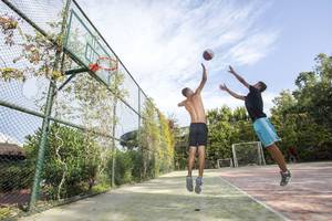 Zwei Männer springen, um einen Basketball zu werfen, auf einem Außensportplatz.
