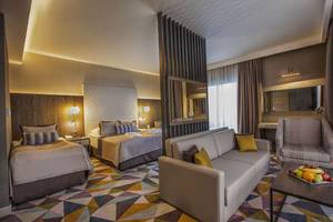 Suite Zimmer im Fame Residence Lara & Spa Hotel mit zwei Betten, Sofa, Tisch und Obstplatte.