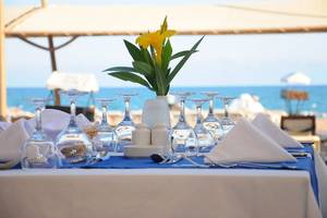 Gedeckter Tisch am Strand mit Blumen in einer Vase und Blick auf das Meer.