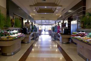 Innenansicht der Halle im Fame Residence Lara & Spa mit Früchtebuffets und beleuchteten Wegen.