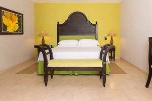 Ein farbenfrohes Schlafzimmer im Occidental Papagayo Hotel mit gelben Wänden, einem großen Bett und Nachttischen.