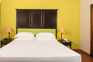 Hotelzimmer im Occidental Papagayo mit gelber Wand, weißem Bett und zwei Nachttischen mit Lampen und Telefonen.